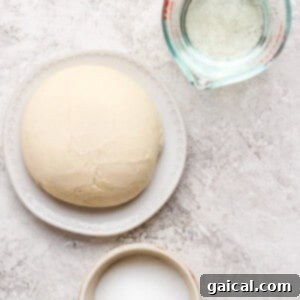 Dough ball on a plate, a measuring cup with water, and a bowl of sugar on a textured surface, ready for preparation.
