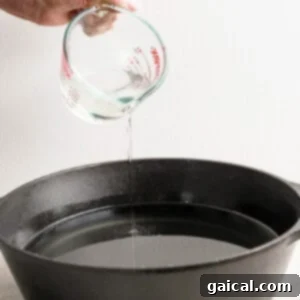 A hand carefully pouring liquid from a measuring cup into a black cast iron pan, preparing for frying.