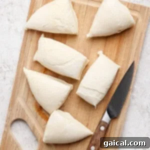 Six pieces of dough are neatly placed on a wooden cutting board next to a knife, showing the prepared dough ready for cooking.