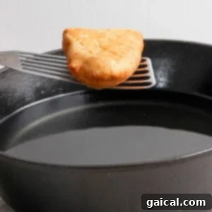 A golden-brown hash brown is being carefully lifted on a spatula over a black frying pan, indicating the frying process.