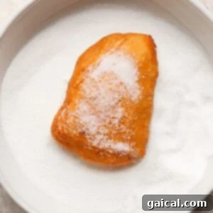 A sugar-covered pastry sits on a plate filled with granulated sugar, demonstrating the coating process.