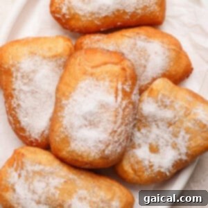 A plate of six sugar-dusted beignets on a white dish, beautifully presented and ready to eat.