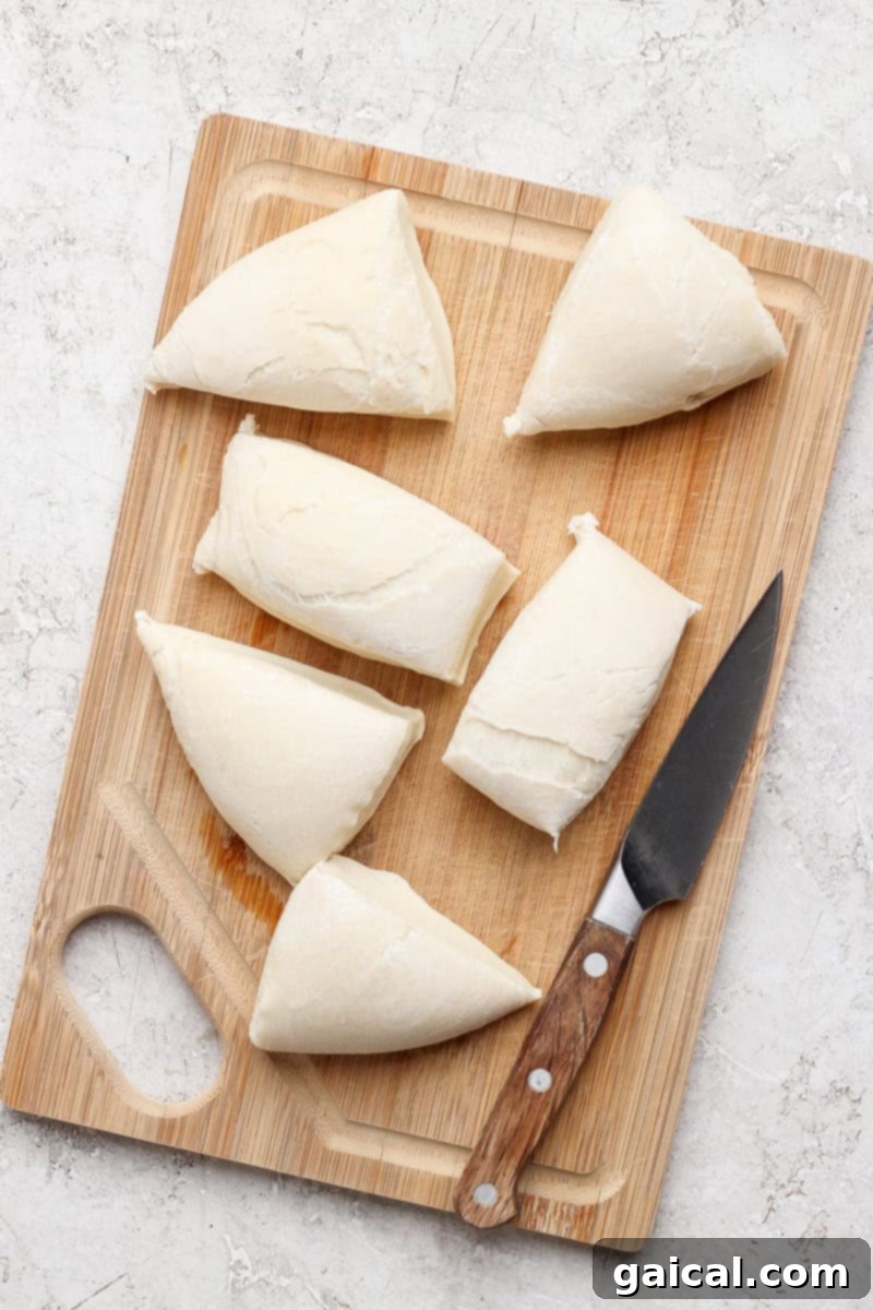 Nonna Marie's Crispy Fried Pizza 4 Sliced triangles of dough are arranged neatly on a wooden cutting board, with a knife resting beside them, ready for frying.