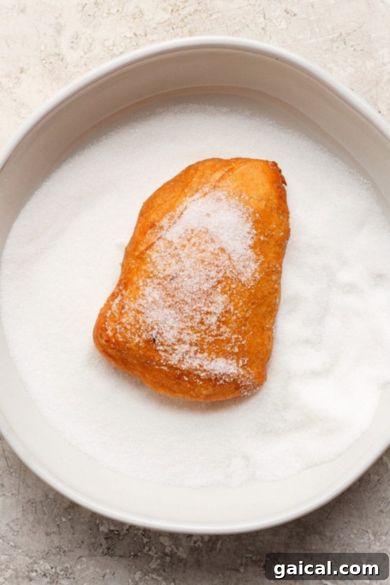 Nonna Marie's Crispy Fried Pizza 7 A freshly air-fried, sugar-covered pastry rests on a plate generously filled with granulated sugar, ready for serving.