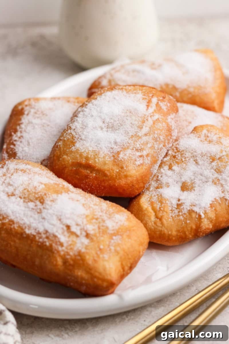 Nonna Marie's Crispy Fried Pizza 8 A plate of perfectly rectangular beignets generously coated with powdered sugar, resting on a light-colored surface, ready to be enjoyed.