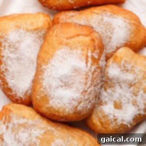 A pile of sugared beignets on a white surface, perfectly golden and inviting.