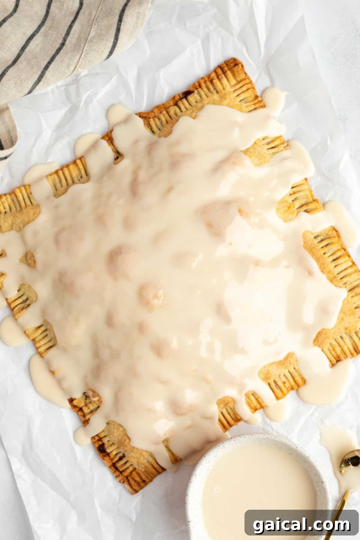 Fueling Frosted Pastries 6 A single large, iced protein pastry with crimped edges rests on crinkled parchment paper, with a small bowl of extra icing beside it.