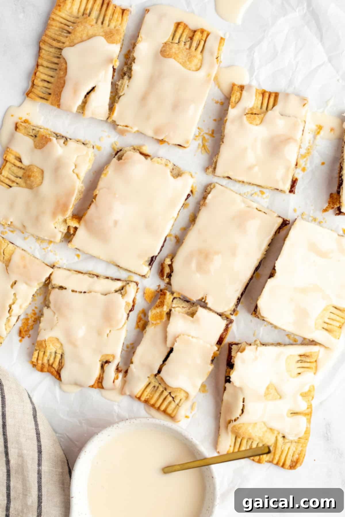 Fueling Frosted Pastries 7 A delightful arrangement of nine iced, rectangular protein pastries on parchment paper, ready to be enjoyed. A small bowl of extra icing is visible.