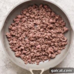 A frying pan containing cooked ground beef on a textured gray background.