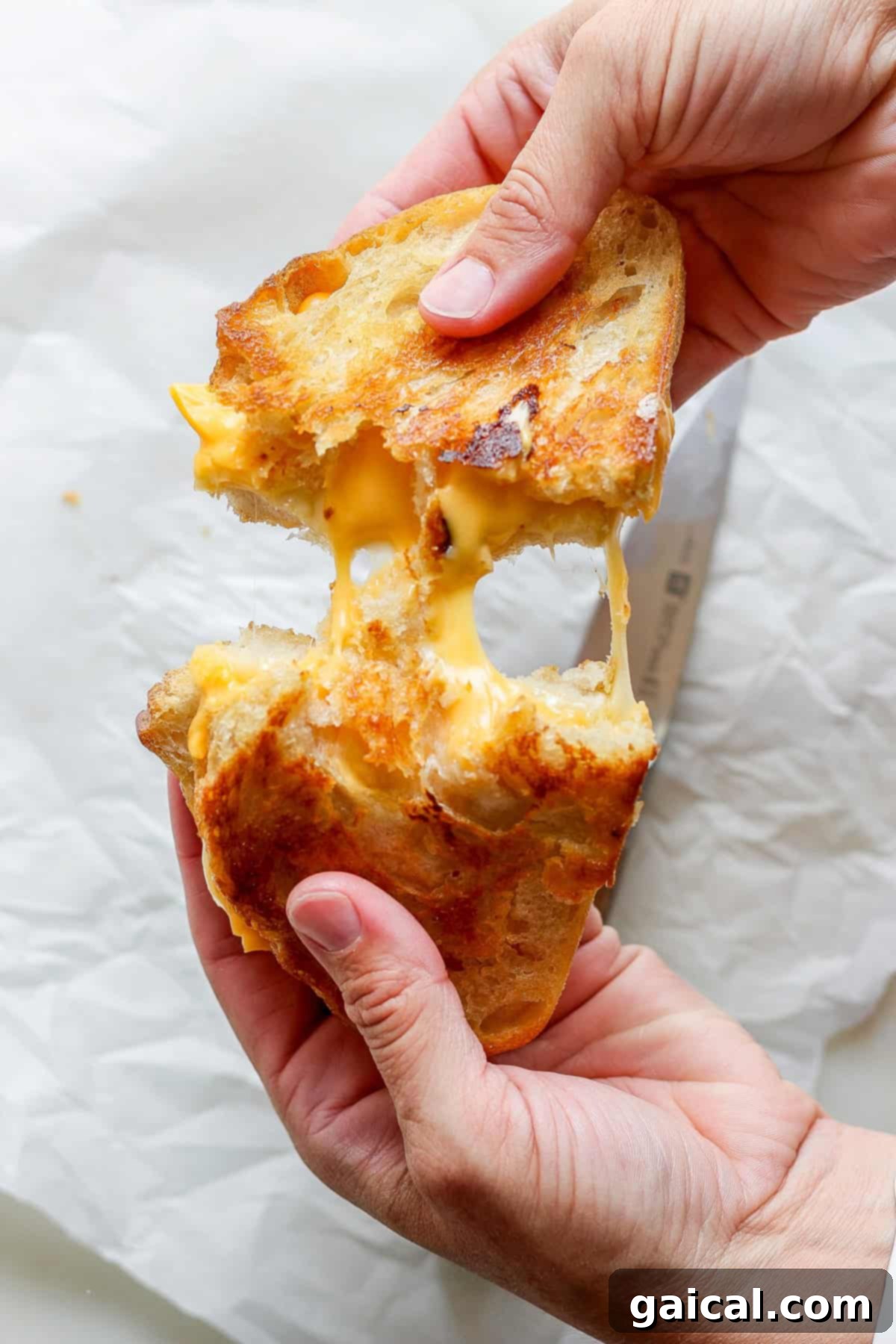 Hands pulling apart a grilled cheese sandwich, with melted cheese stretching between the toasted bread slices, perfectly paired with a warm bowl of tomato soup.