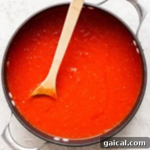 A pot filled with rich, red tomato sauce and a wooden spoon resting inside evokes the comforting aroma of grilled cheese and tomato soup on a light-colored surface.