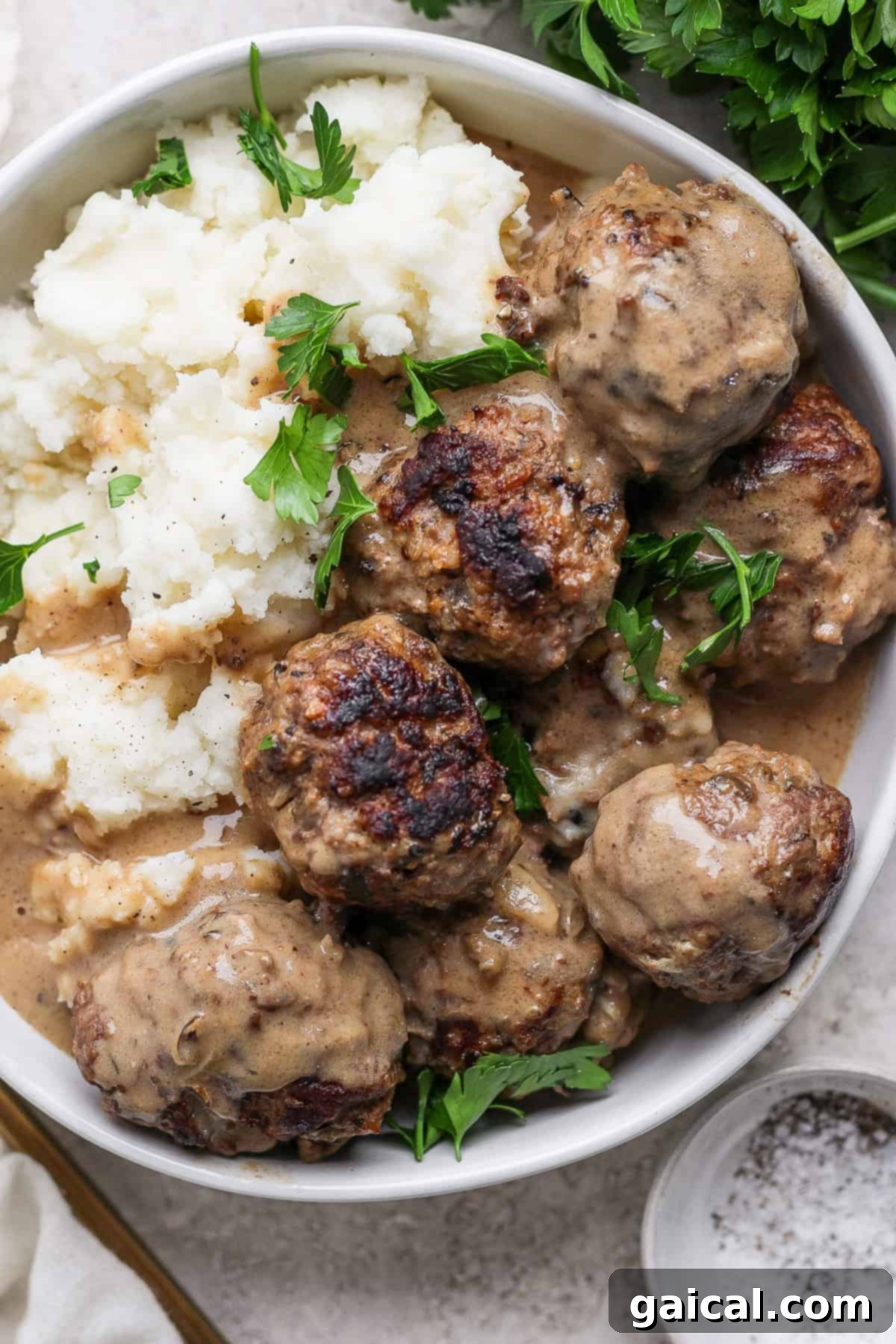North Star State Swedish Meatballs 2 A serving of Minnesota Swedish Meatballs in a rich, creamy sauce, alongside fluffy mashed potatoes and garnished with fresh parsley.