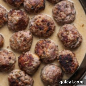 A skillet containing several browned meatballs simmering contentedly in a rich, creamy gravy, ready for final cooking.