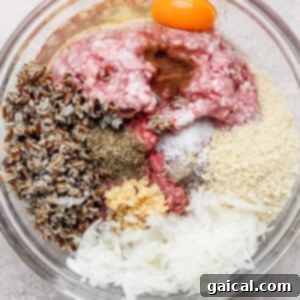 A glass bowl containing a mix of ground meat, an egg, wild rice, spices, breadcrumbs, minced garlic, and shredded onions, ready for mixing into meatballs.
