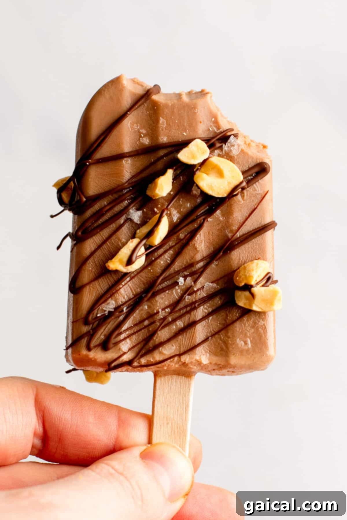 Guilt-Free Protein Fudge Pops 8 Person holding a chocolate popsicle with drizzled chocolate and peanut pieces, partially eaten.