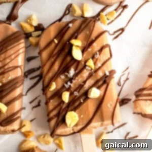 Chocolate-coated ice cream bar sprinkled with nuts and drizzled chocolate on parchment paper.