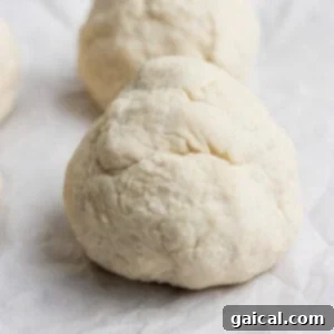Close-up of two smooth dough balls resting neatly on parchment paper, awaiting the next step in the baking process.