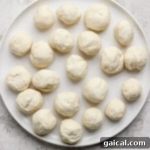 A white plate neatly displays 20 raw, evenly spaced dough balls, ready for the next step of the recipe preparation.