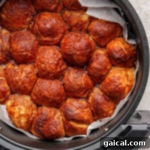 Perfectly golden brown pull-apart bread rolls, tightly packed in a round air fryer container lined with parchment paper, fresh out of the air fryer.