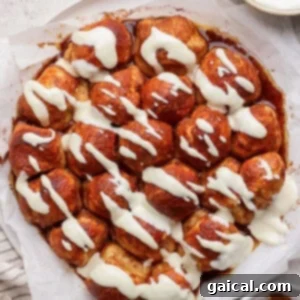 A round, golden cinnamon pull-apart bread, beautifully topped with a swirl of cream cheese icing, sits on parchment paper, accompanied by a bowl of icing and a dish of cinnamon.