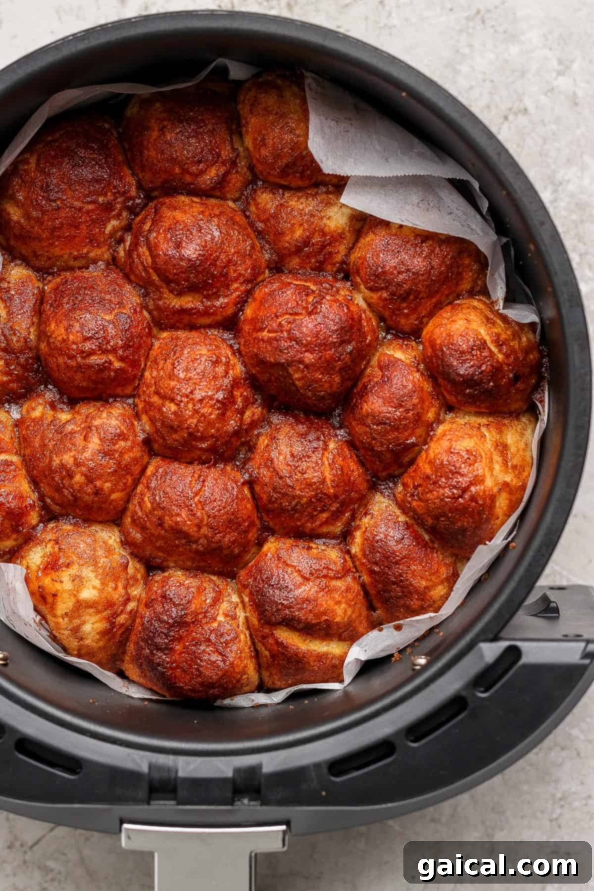 A round air fryer basket filled with perfectly golden brown pull-apart bread rolls, nestled in parchment paper.