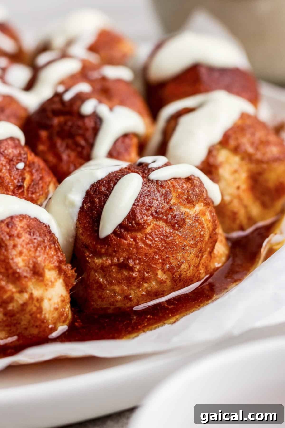 A close-up view of fluffy cinnamon rolls, generously topped with a decadent white cream cheese icing, arranged enticingly on wax paper.