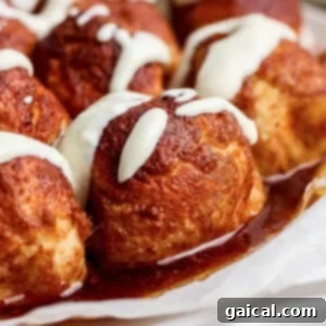 Close-up of golden cinnamon rolls, glistening with white icing and a syrup drizzle, presented on a round plate.