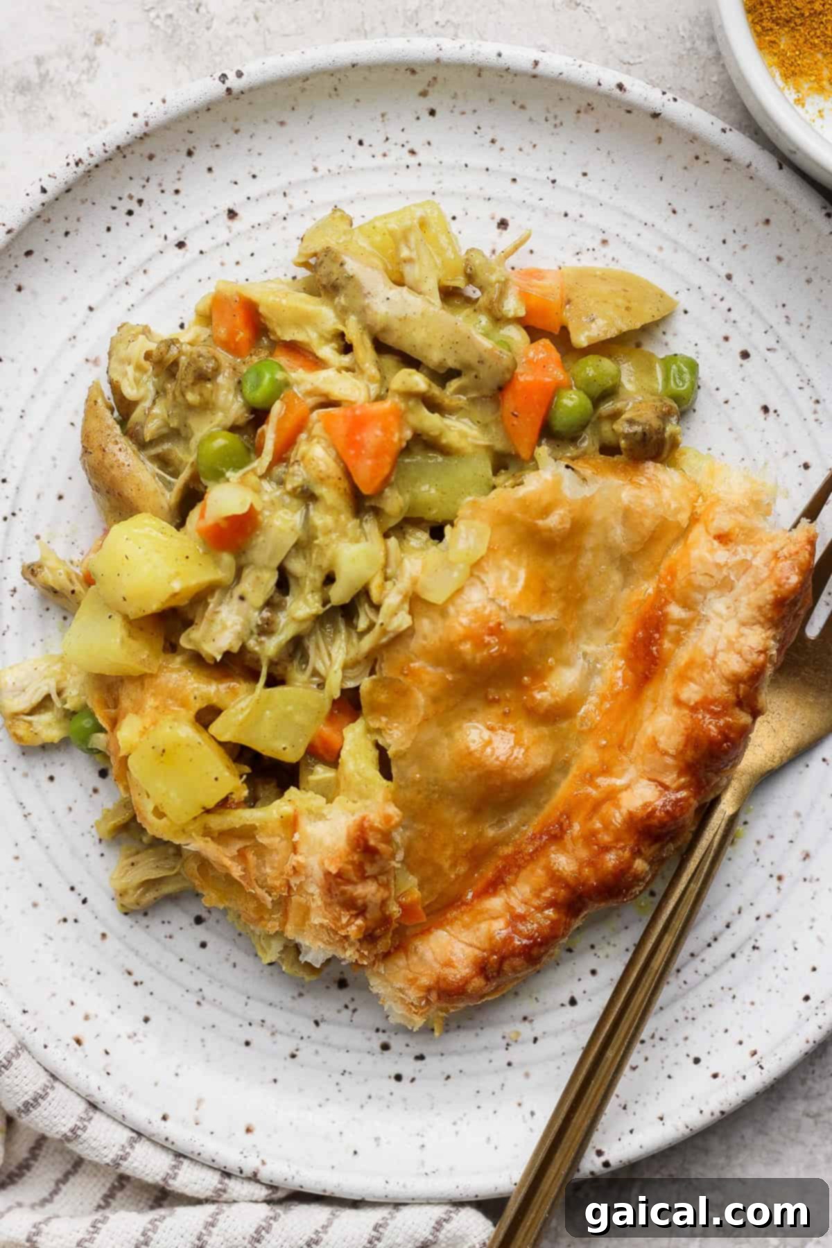 A slice of chicken pot pie with vegetables on a speckled plate, accompanied by a fork and a knife.