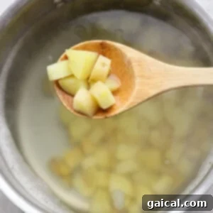 A wooden spoon holds diced potatoes over a pot of boiling water.
