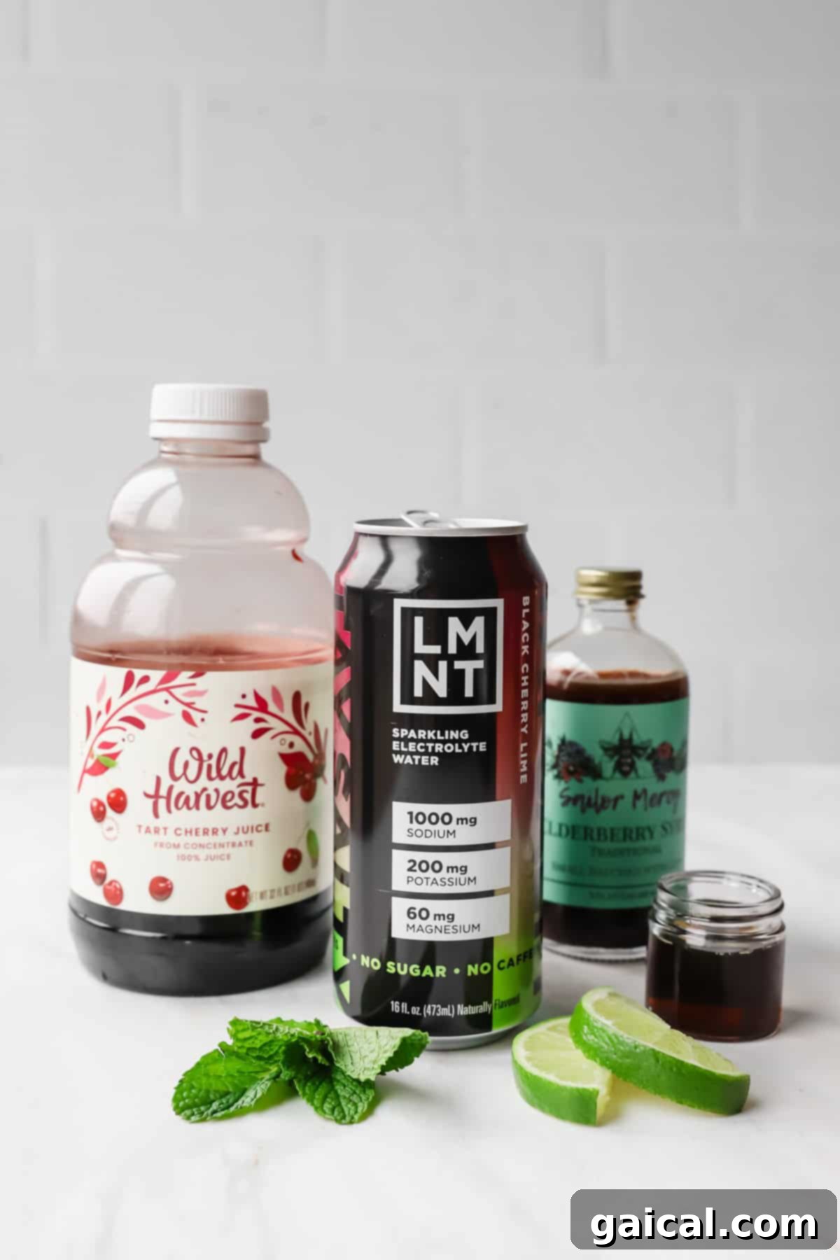 Nighttime Nectar 3 A bottle of tart cherry juice, a can of LMNT electrolyte drink, elderberry syrup, mint leaves, and lime slices on a white surface.