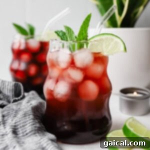 Nighttime Nectar 7 Two glasses of iced berry drink with lime slices and mint, placed on a table with a striped cloth. A small candle and lime wedges are nearby, with a potted plant in the background.