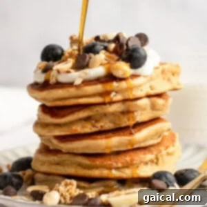 Power-Packed Pancakes 6 A stack of pancakes topped with blueberries, granola, yogurt, chocolate chips, and syrup being poured over them.