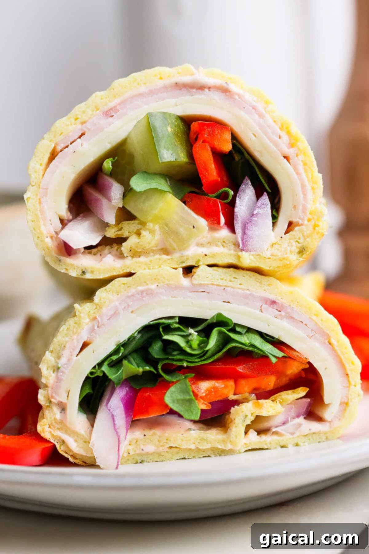 Protein-Packed Cottage Cheese Wraps 2 Close-up of two sandwich halves stacked, featuring layers of turkey, cheese, spinach, tomato, onion, and green pepper on a rolled flatbread. Resembling cottage cheese wraps in their wholesome appeal, they rest invitingly on a white plate.