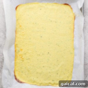 A rectangular sheet of pale yellow flatbread on parchment paper, placed on a baking tray.