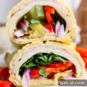 Close-up of a tortilla wrap cut in half, filled with turkey, cheese, lettuce, red onion, and bell peppers, on a white plate.