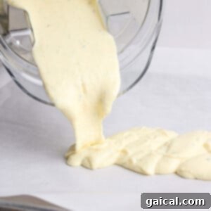 Thick yellow batter is being poured from a blender onto a lined baking sheet.