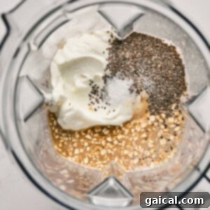 All the base ingredients for the blended oats, including yogurt, chia seeds, salt, oats, and a liquid, are being poured into a blender.