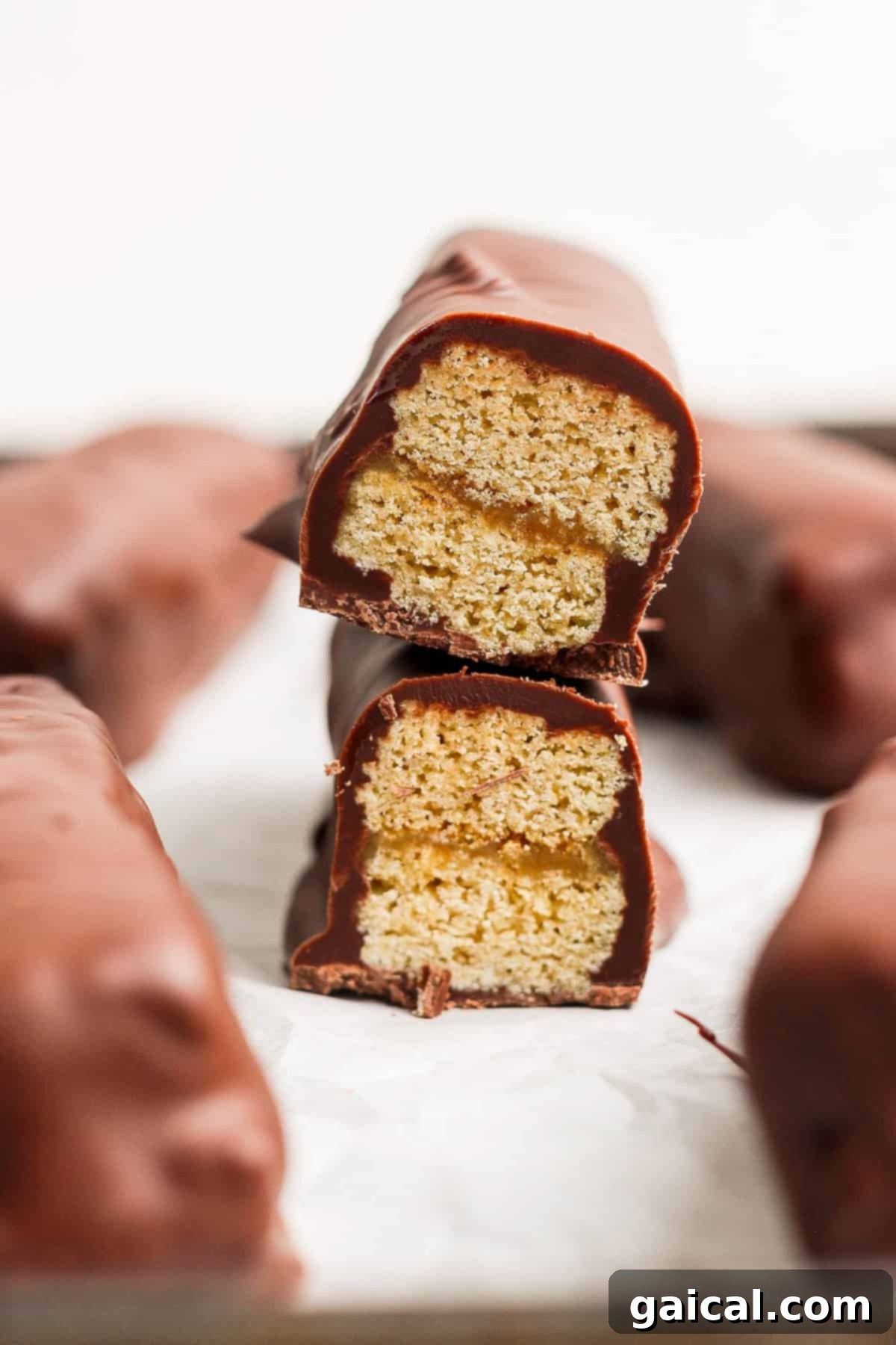 Protein-Packed Peanut Butter Twix Bars 2 Two chocolate-coated biscuit bars stacked with one bisected, revealing a layered interior on a white surface.