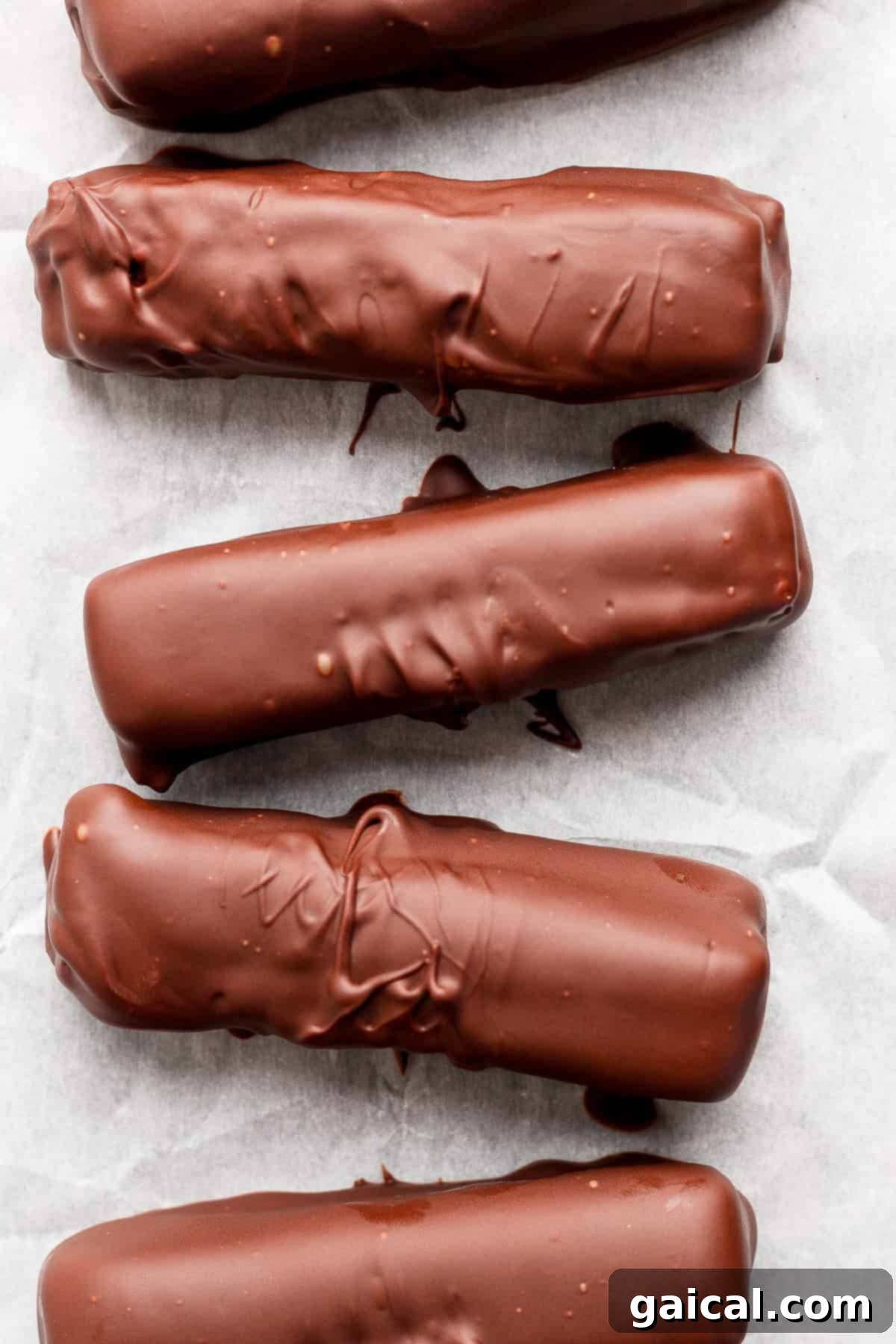 Protein-Packed Peanut Butter Twix Bars 5 Five chocolate-coated bars arranged in a row on parchment paper.