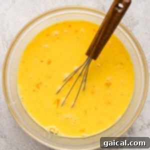 Buttery Croissant Egg Bake 10 A whisk in a clear glass bowl containing perfectly beaten eggs, ready to be incorporated into the casserole.