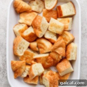 Buttery Croissant Egg Bake 6 A white baking dish filled with bite-sized croissant pieces ready to form the base of the casserole.