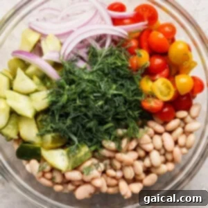 Zesty Dill Pickle White Bean Salad 9 Glass bowl with sliced red onions, halved cherry tomatoes, cucumber chunks, white beans, and a mound of fresh dill.