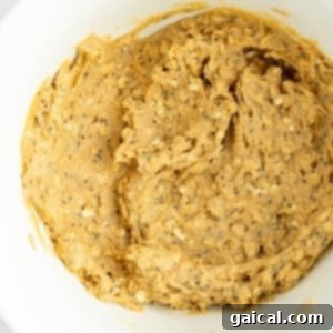 Creamy peanut butter and chia seed mixture being stirred in a white bowl, demonstrating the perfect consistency for the oat base.