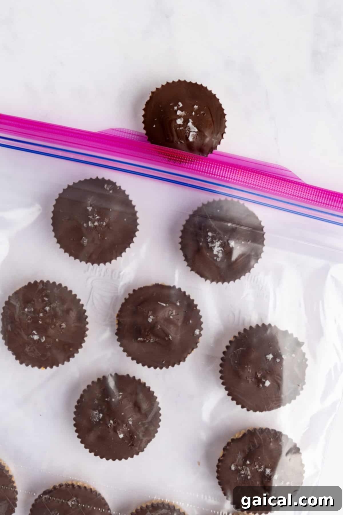 Chocolate cups with a sprinkle of sea salt on top are neatly arranged inside a transparent resealable bag, with one cup placed artfully above the bag, ready for storage.