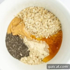 A white bowl containing a mix of oats, peanut butter, chia seeds, protein powder, and honey, ready to be combined.