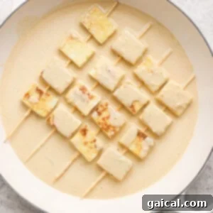 Skewered tofu cubes in creamy marinade on a round white dish.