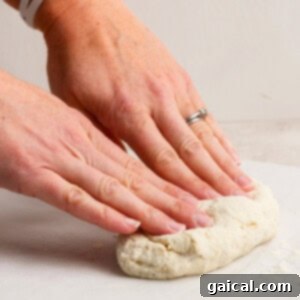 Hands with a watch and ring kneading dough on a white surface.