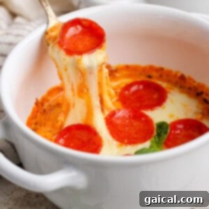 Personal Cottage Cheese Pizza Bowl 7 A spoon lifts cheesy pepperoni pizza dip from a white bowl. Fresh basil leaves are visible nearby.