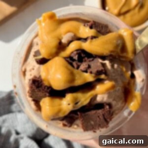 A bowl of chocolate ice cream topped with caramel sauce and chunks of chocolate brownies. A gold spoon is partially visible on the right.
