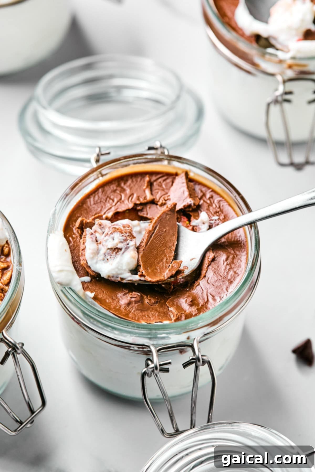 Create Your Own Magical Chocolate Coating 2 Spoon dipping into a glass jar of chocolate mousse with visible layers of cream and chocolate. Other jars are partially visible in the background.